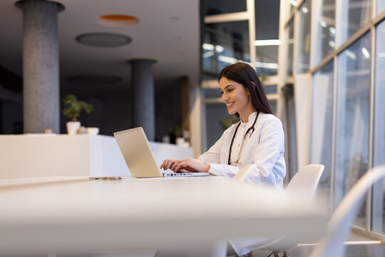 Professional female physician working on laptop, analyzing medical data while standing in contemporary healthcare setting