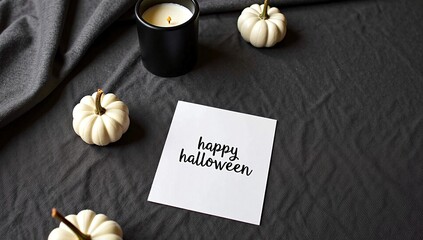 Stylish flat lay of a Happy Halloween greeting card surrounded by mini white pumpkins and a candle on a dark background