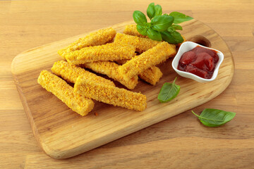 Cheese sticks with basil and ketchup on a wooden table.