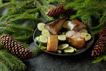 Smoked mackerel with fresh cucumber and green onions on a black plate.