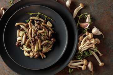 Fried shimeji mushrooms with thyme and garlic on a black plate.