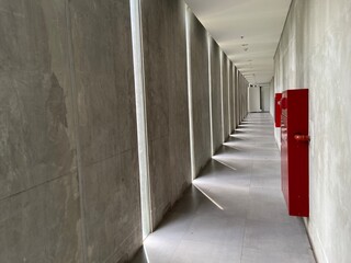 Minimalist corridor interior with concrete walls, emergency exit sign, and fire safety equipment in...