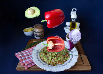 Delicious homemade guacamole, with vegetables such as guacamole, bell pepper, and red onion falling into the dish.