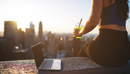 Woman holding smoothie with laptop on rooftop.