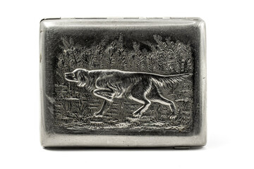 An old silver cigarette case with a bas-relief of an Irish setter hunting among the grass. The dog points in the direction of the target. Scratches are visible on the surface.