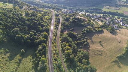 Aerial view of railway tracks curving through green forest and farmland with rural village in the...