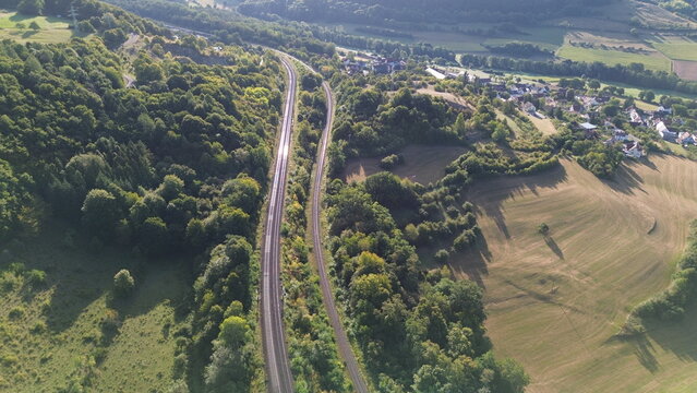 Aerial view of railway tracks curving through green forest and farmland with rural village in the background