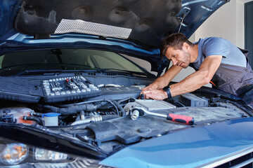Male mechanic using socket wrench to repair car engine in garage. Man with repair tools in hands...