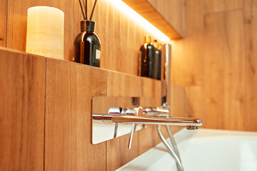 Modern chrome bathtub faucet with shower head mounted on wall with decorative candle and bottles....