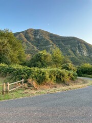 Start of a Hike in Castagno d’Andrea – Sunlit Mountain and Lush Forest at Day’s End, with Wooden Fence Framing the Trailhead in Tuscany’s Apennines, Capturing a Peaceful Summer Evening