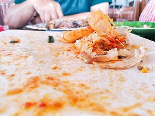 shrimp shells, oil stains, and sauce on dirty white plates after finishing a meal at a seafood...