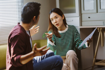 Frustrated Asian couple arguing over paperwork and expenses, expressing their worries about...