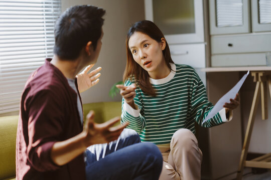 Frustrated Asian couple arguing over paperwork and expenses, expressing their worries about financial problems and mounting debt at home