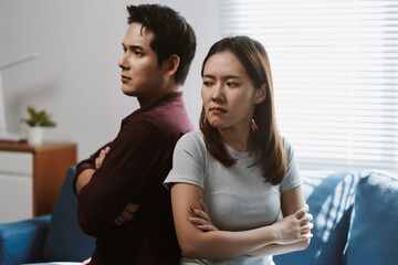 Asian couple experiencing conflict, feeling angry and upset while ignoring each other, highlighting relationship issues and tension at home