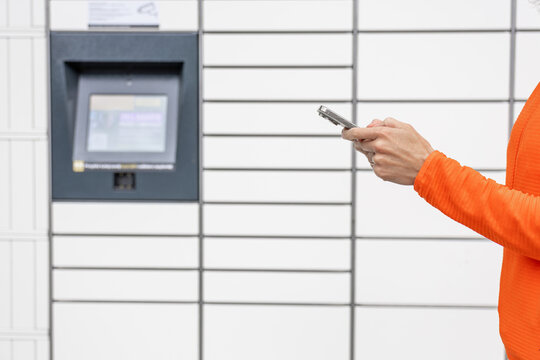 Hand holding mobile phone to scan parcel code at lockerbox. Package retrieval, contactless delivery, self service, online shopping, smart locker technology.