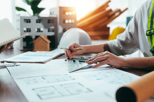 Architect working on blueprint project using a ruler and set square, with building models and other documents on the desk