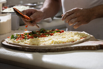 Chef pizzaiolo prepara uma pizza temperando com molho de tomate, manjericão e queijo