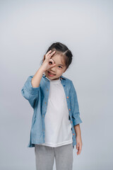 Happy child playing with playful expression while wearing casual outfit and standing against a...