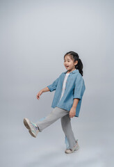 Playful child in casual outfit joyfully walking against a neutral background, showcasing carefree...