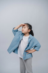 Thoughtful Asian girl posing in casual outfit with blue shirt, white t-shirt, and grey pants,...