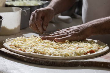 Chef pizzaiolo prepara uma pizza adicionando queijo mussarela