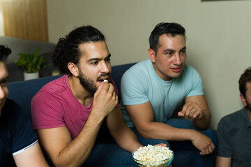 Group of friends watching sports and eating popcorn at home