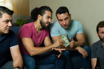 Male friends betting money while watching sports at home