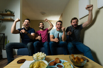 Wide angle view of friends cheering and drinking beer while watching sports at home