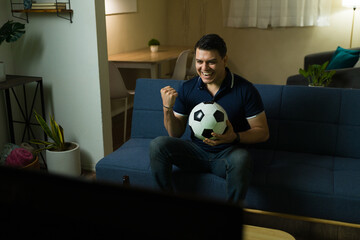 Excited sports fan celebrating goal while watching soccer match at home