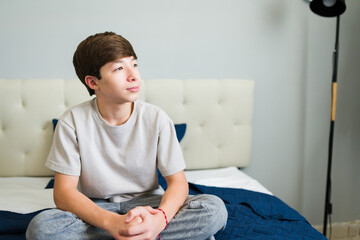 Thoughtful teenager sitting on bed in modern bedroom