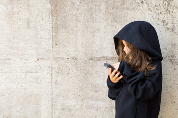 Lonely young man with mobile phone in front of a gray wall