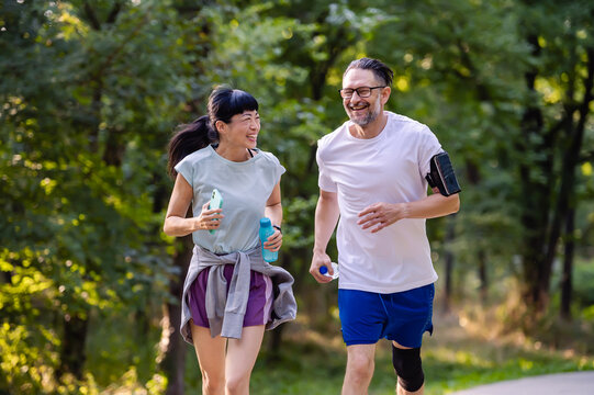Smiling diverse middle-aged couple jogging on a park trail, enjoying outdoor exercise, healthy lifestyle, and spending active time together in nature