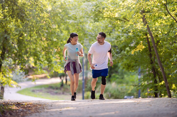 Fototapeta premium Smiling diverse middle-aged couple jogging on a park trail, enjoying outdoor exercise, healthy lifestyle, and spending active time together in nature