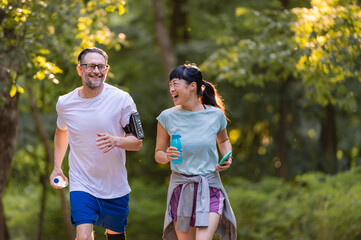 Happy diverse middle-aged couple jogging together in park, smiling and talking while exercising outdoors, enjoying active lifestyle, health, and fitness in nature