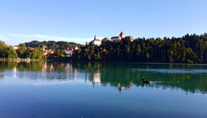 Tranquil lake scene showcasing a town nestled on a hillside, with mirrored reflections of the buildings on the calm water's surface.