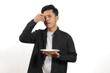 young Asian man dressed in a black shirt is eating something from a plate, holding a spoon. Shot in...