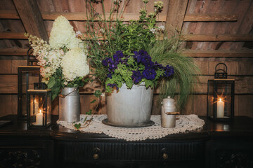 A cozy rustic display featuring metal buckets filled with fresh white and purple flowers, flanked...