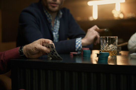 Poker game featuring cigars and assorted drinks on the table
