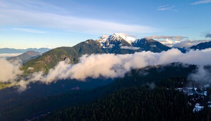 Fototapeta premium A breathtaking vista of snow-capped mountains rising above a valley shrouded in swirling clouds, showcasing the rugged beauty of nature's grandeur.