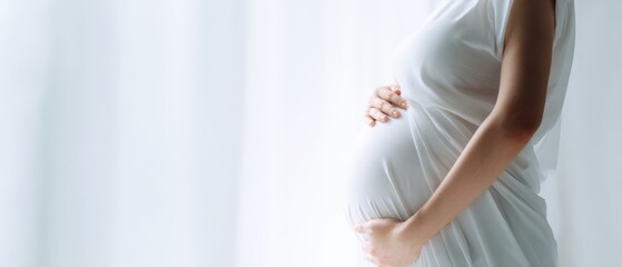 The pregnant woman cradling her belly in soft white draped maternity portrait