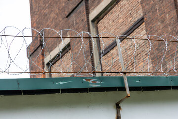 Close-up of barbed wire security fence with rusty support and brick industrial wall in background