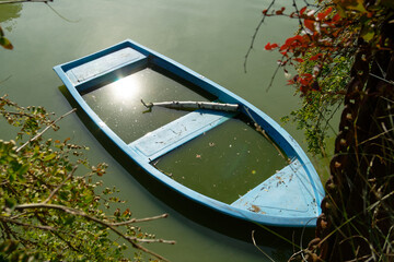 A blue boat floats serenely on a calm lake, reflecting the sunlight and surrounded by greenery.