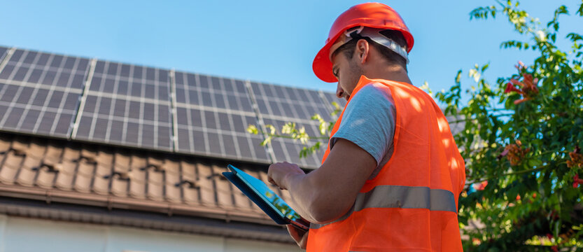 Engineer with Tablet Inspecting Solar Panels on Roof