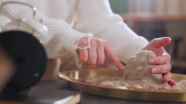 Hand view of explorer shaping octopus from soft moldable material in tray during therapy session, highlighting mindful sculpting process and delicate hand positioning in warm indoor setting