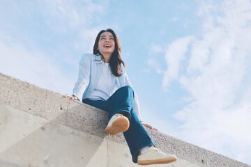 Cheerful young Asian woman sitting  on the roof under blue sky background.
