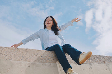 Cheerful young Asian woman sitting  on the roof under blue sky background.