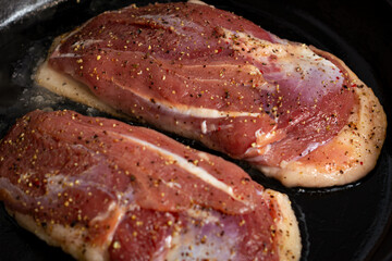 two duck breasts are fried in a pan, seasoned with salt and a mixture of peppers