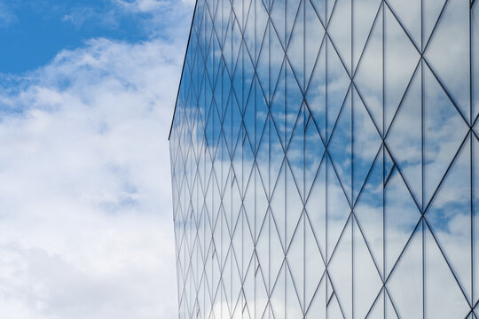 Fragment of a glass building with a reflecting blue sky with clouds. against its background. Modern offices in a skyscraper. High quality photo