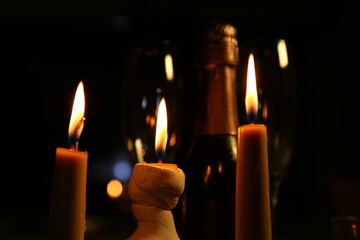Three burning wax candles on a dark background with champagne glasses and bottle behind. Candles...