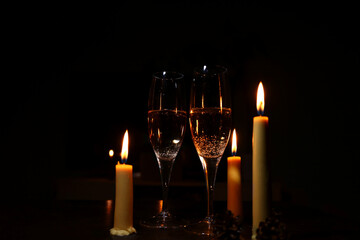 Two champagne glasses with white alcohol wine on three burning wax candles dark background. Candles fire flame with empty copy space. Happy romantic party celebration. Closeup atmosphere Christmas